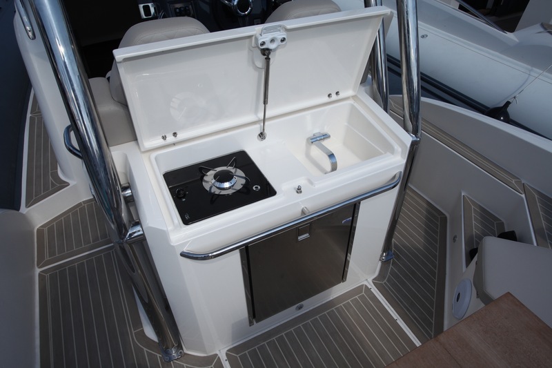 Adossé au siège de pilotage et encadré par les supports inox du T-top, le bloc-cuisine comporte l'essentiel pour la petite croisière : réchaud à gaz, évier, réfrigérateur.
