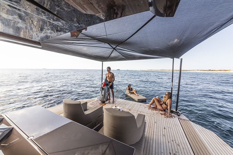 Au mouillage, les pavois se rabattent sur l’eau augmentant la surface du cockpit arrière. Un ample taud ajouré permet de limiter l’impact des UV et laisse passer l’air.

