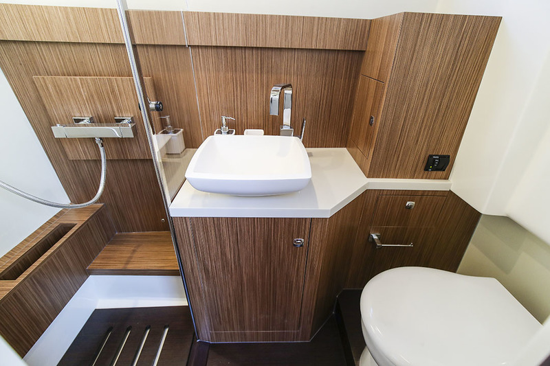 Grande salle d’eau avec cabine de douche. Outre le lavabo et le WC marin électrique, on trouve quelques rangements utiles et un grand hublot avec ouvrant.